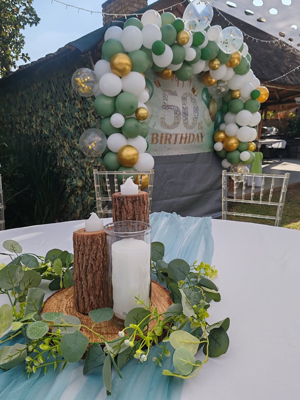 Round table with a candle centrepiece and a green and gold 50th balloon arch